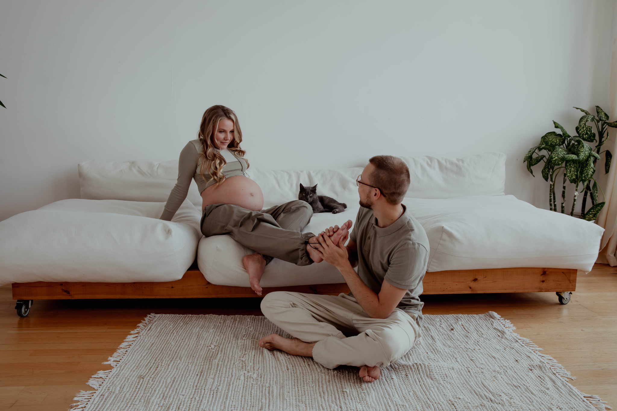 A man massages feet of a pregnant woman in a bright apartment